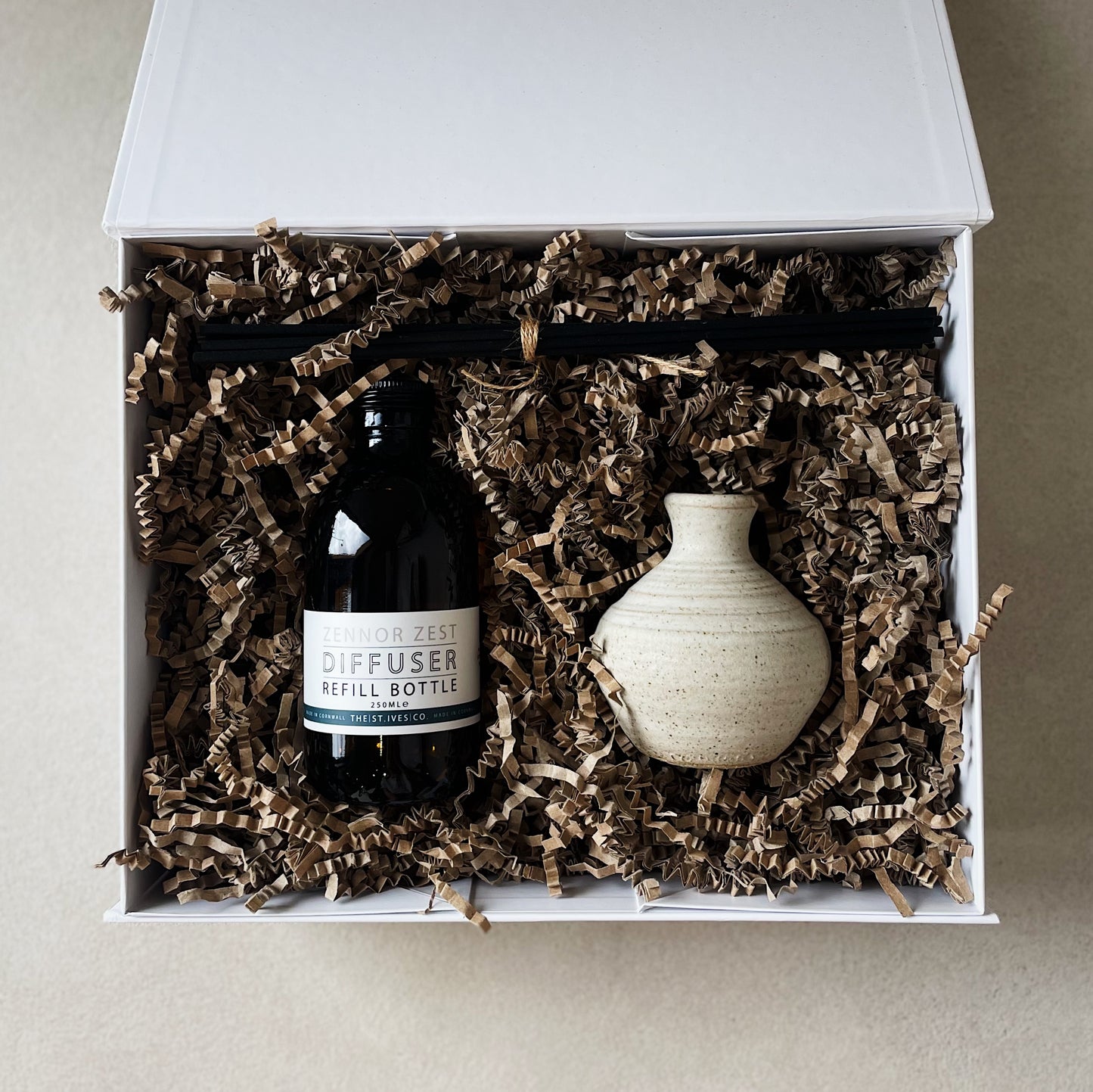 A white Quality Hamper box filled with Zennor Zest 250ml refill diffuser oil + a hand made posy pot with reeds. Made in Cornwall.