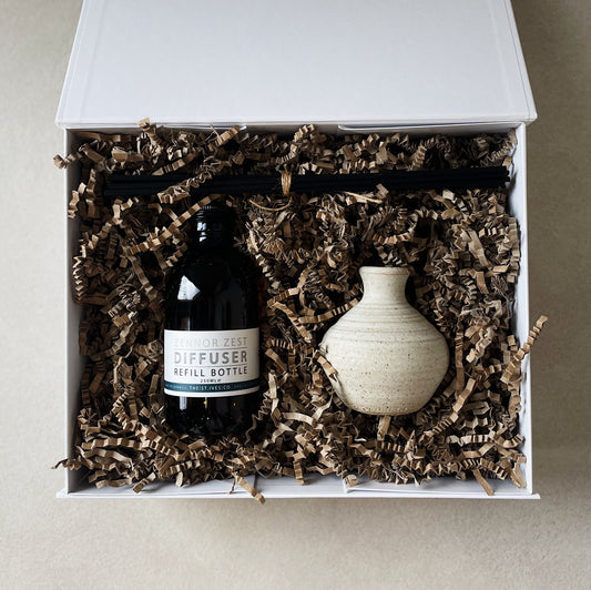 A white Quality Hamper box filled with Zennor Zest 250ml refill diffuser oil + a hand made posy pot with reeds. Made in Cornwall.